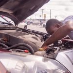 A man is performing car maintenance in a parking lot.
