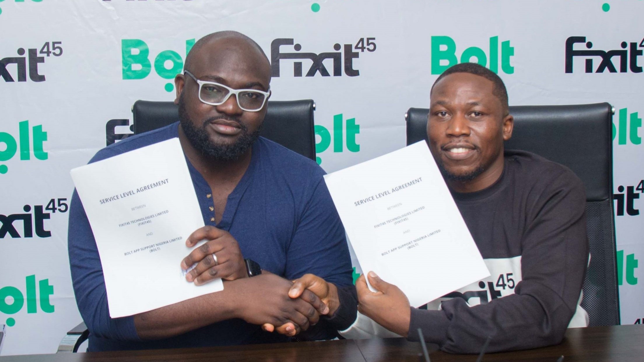 Two men at a table holding up papers.