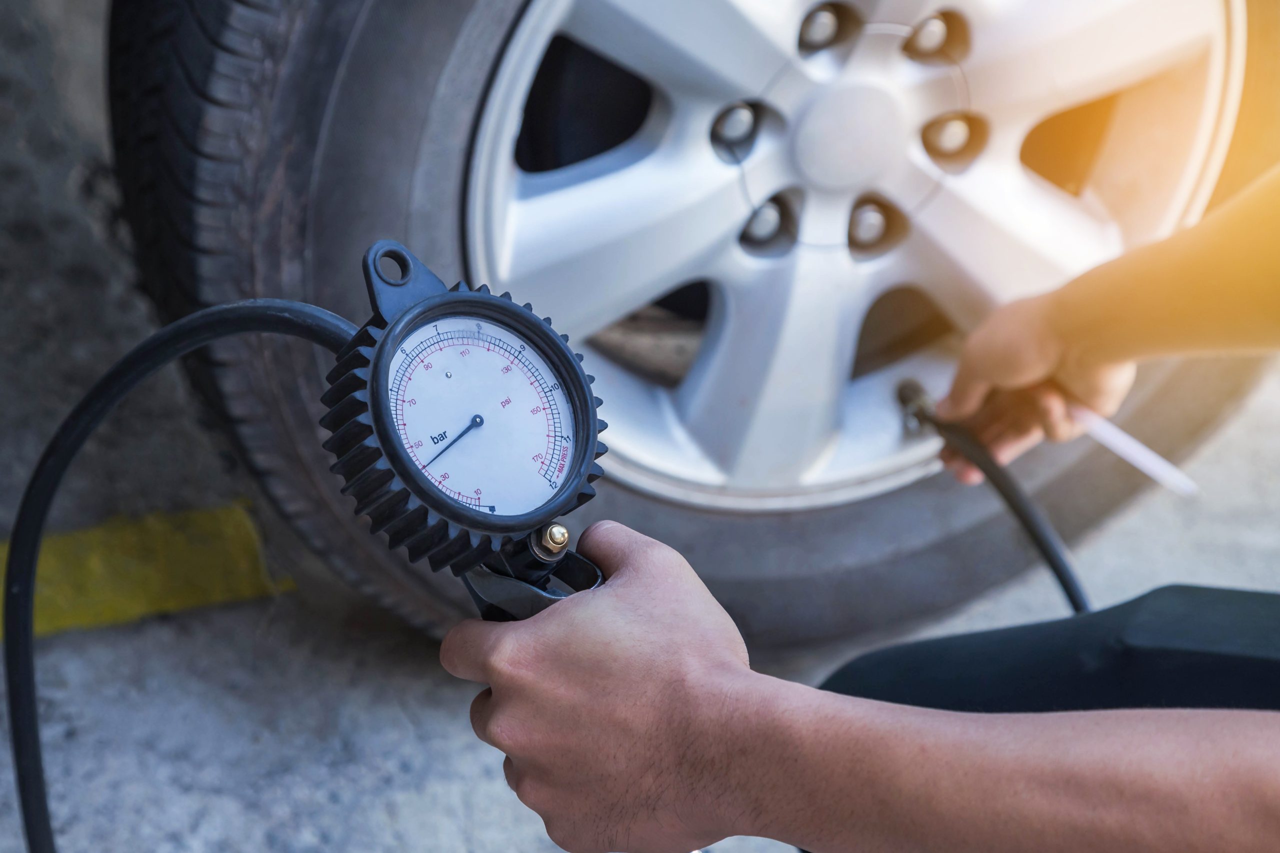 A person checking the air pressure of a car tire using a pressure gauge tool in daylight.