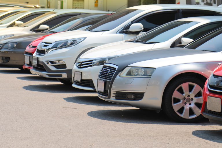 Closeup of front side of cars parking in outdoor parking lot beside the street beside the street in bright sunny day.