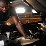 professional car mechanic is examining engine under the hood at auto repair shop, make notes, checking notes in notebook