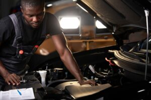 professional car mechanic is examining engine under the hood at auto repair shop, make notes, checking notes in notebook